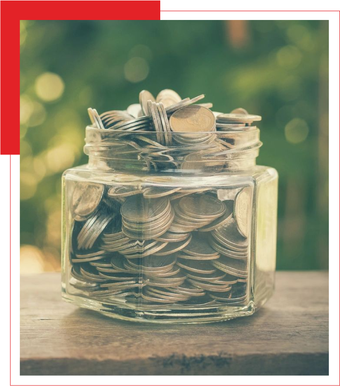 Transparent jar filled with coins on a wooden surface with a blurred green background.